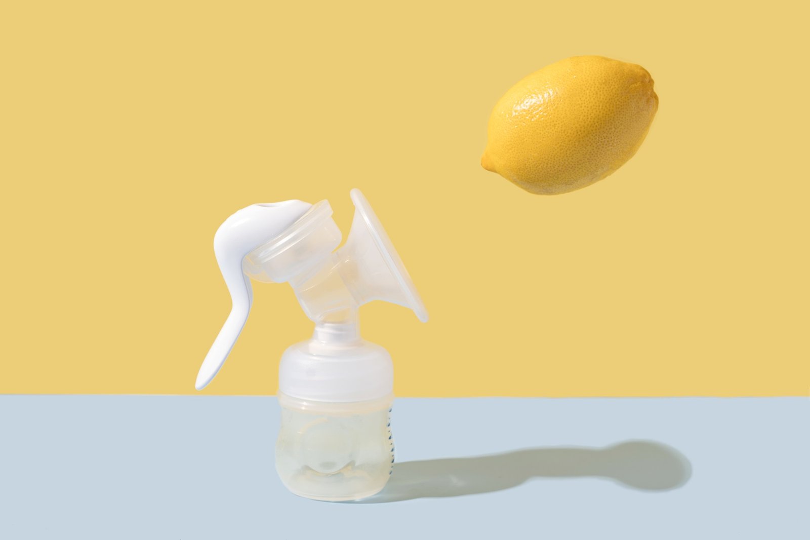 Manual breast pump and lemon on blue background with hard shadows